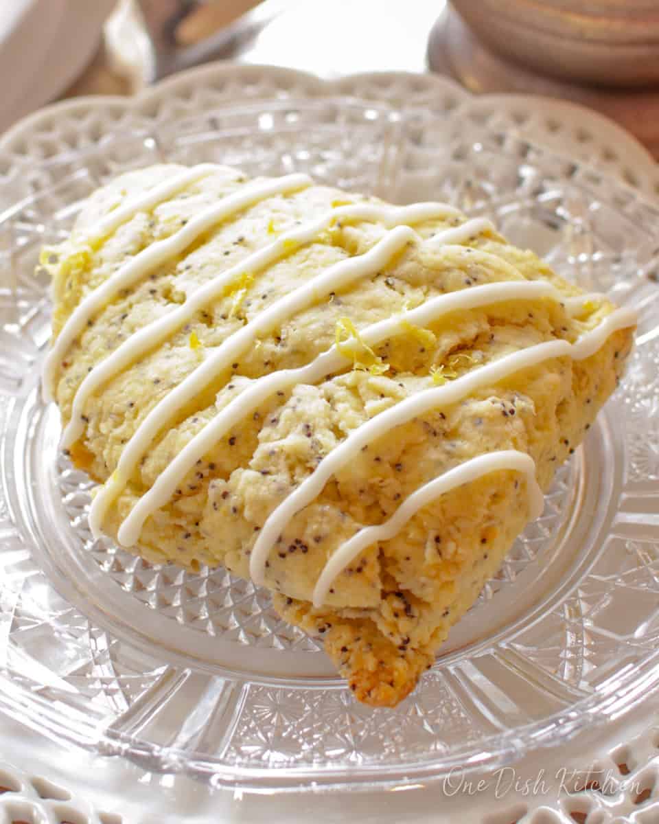 One lemon glazed scone on a plate near a cup of coffee.