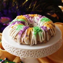 a small king cake topped with a glaze and colored sugar on a mini cake stand