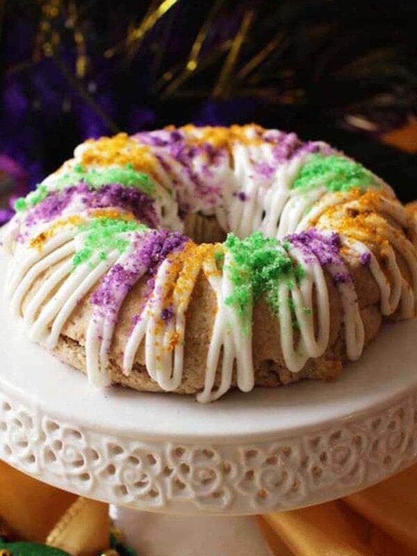 a small king cake topped with a glaze and colored sugar on a mini cake stand