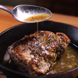pork tenderloin in a cast iron skillet with sauce being poured on top.