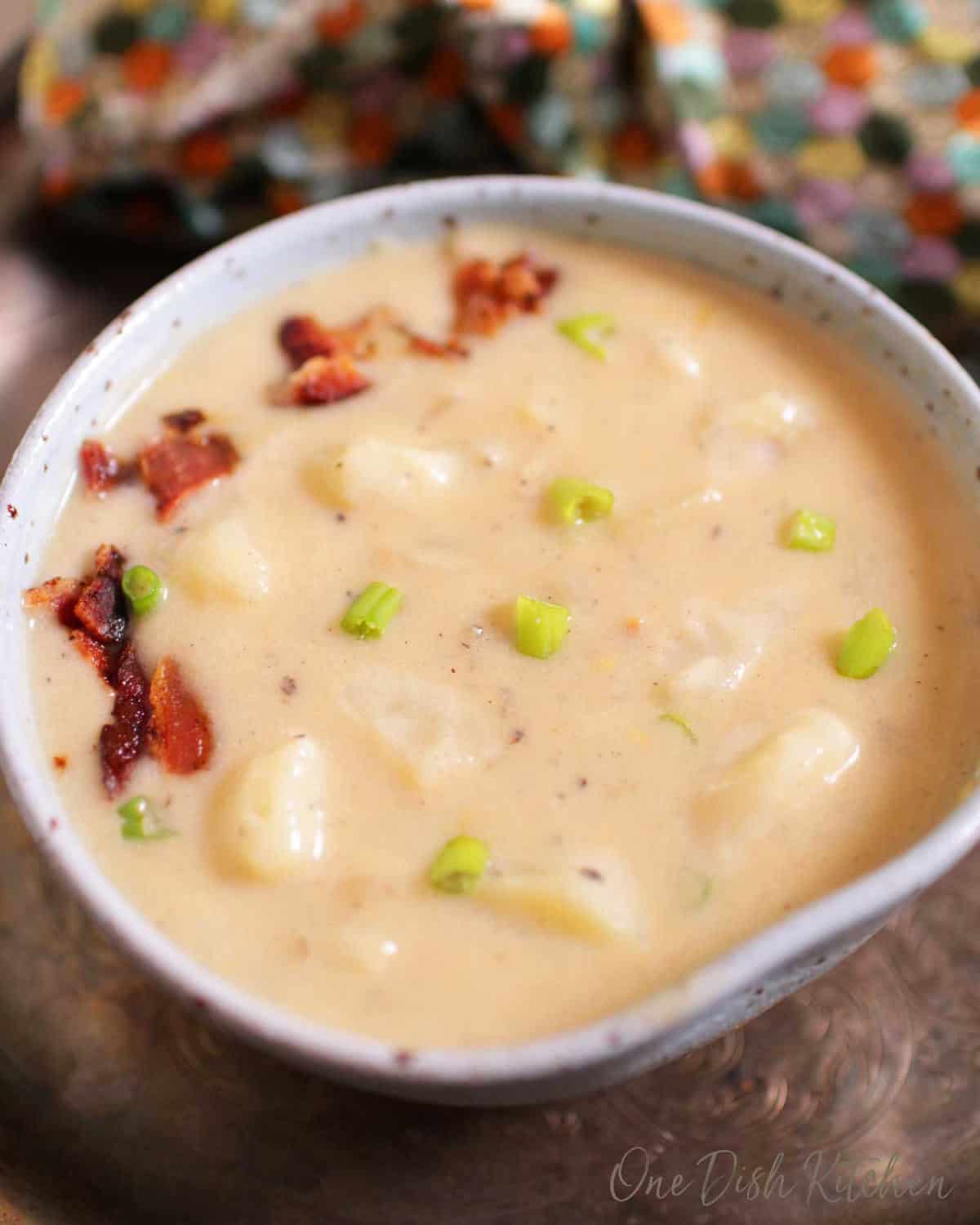 a single serving of potato soup in a blue bowl topped with crumbled bacon.