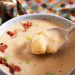 a blue bowl filled with potato soup topped with bacon crumbles.