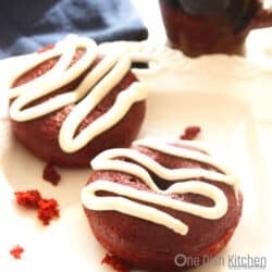 2 frosted red velvet donuts on a white plate.