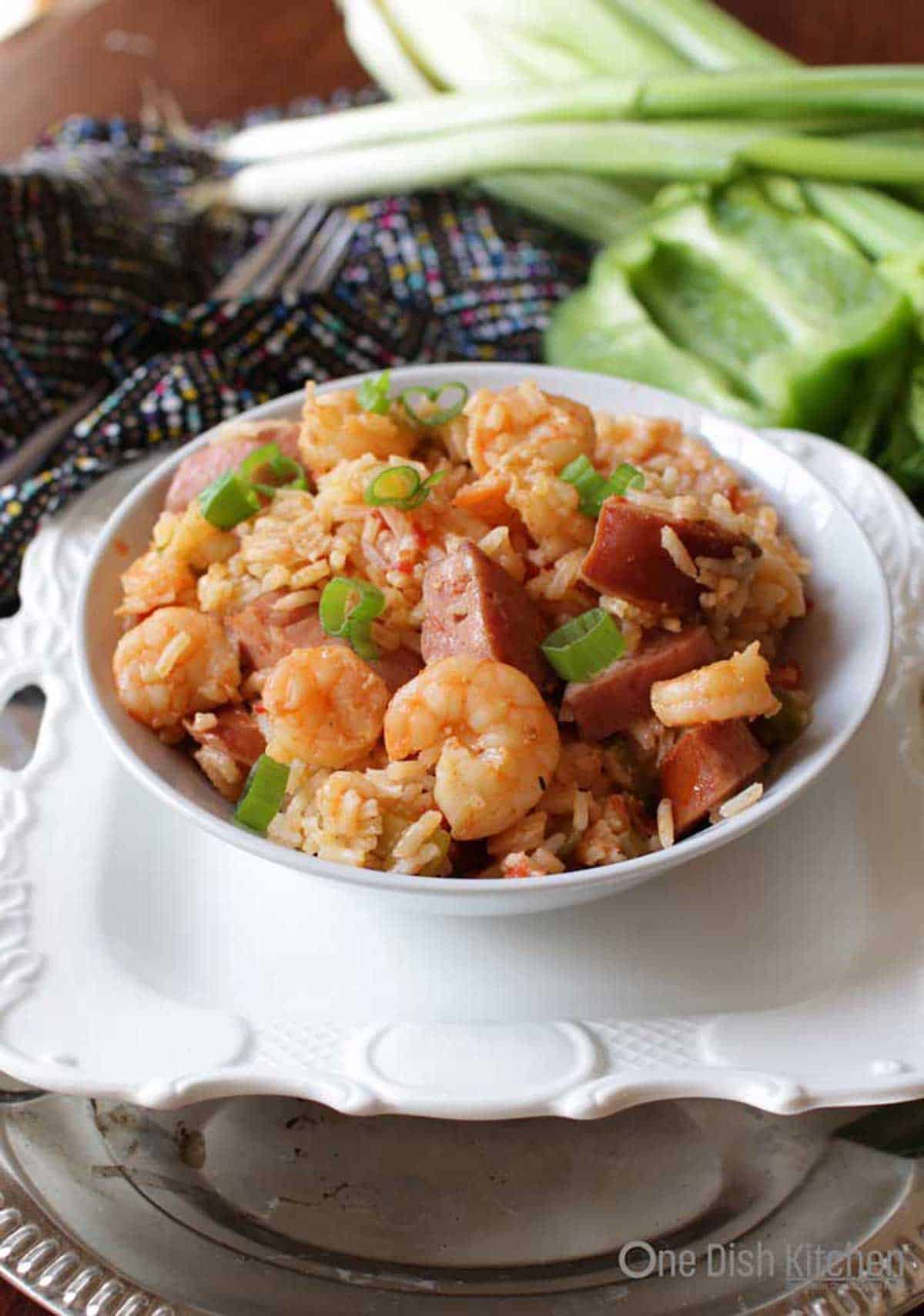 Shrimp and sausage jambalaya in a bowl with onions, celery, and green bell peppers in the background.