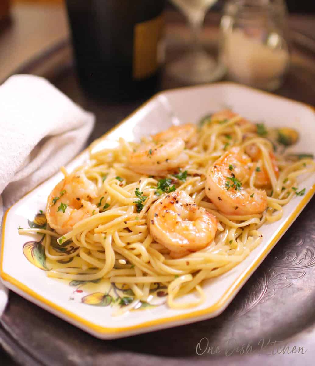 a plate of shrimp scampi next to a glass of champagne.