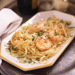 a plate of shrimp scampi on a silver tray next to a brown napkin.