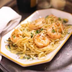 a plate of shrimp scampi next to a glass of champagne.