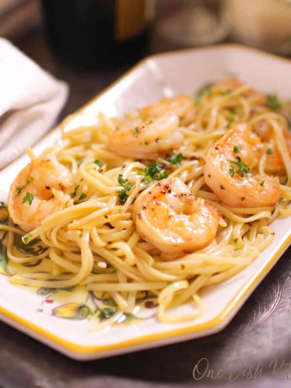 a plate of shrimp scampi next to a glass of champagne.