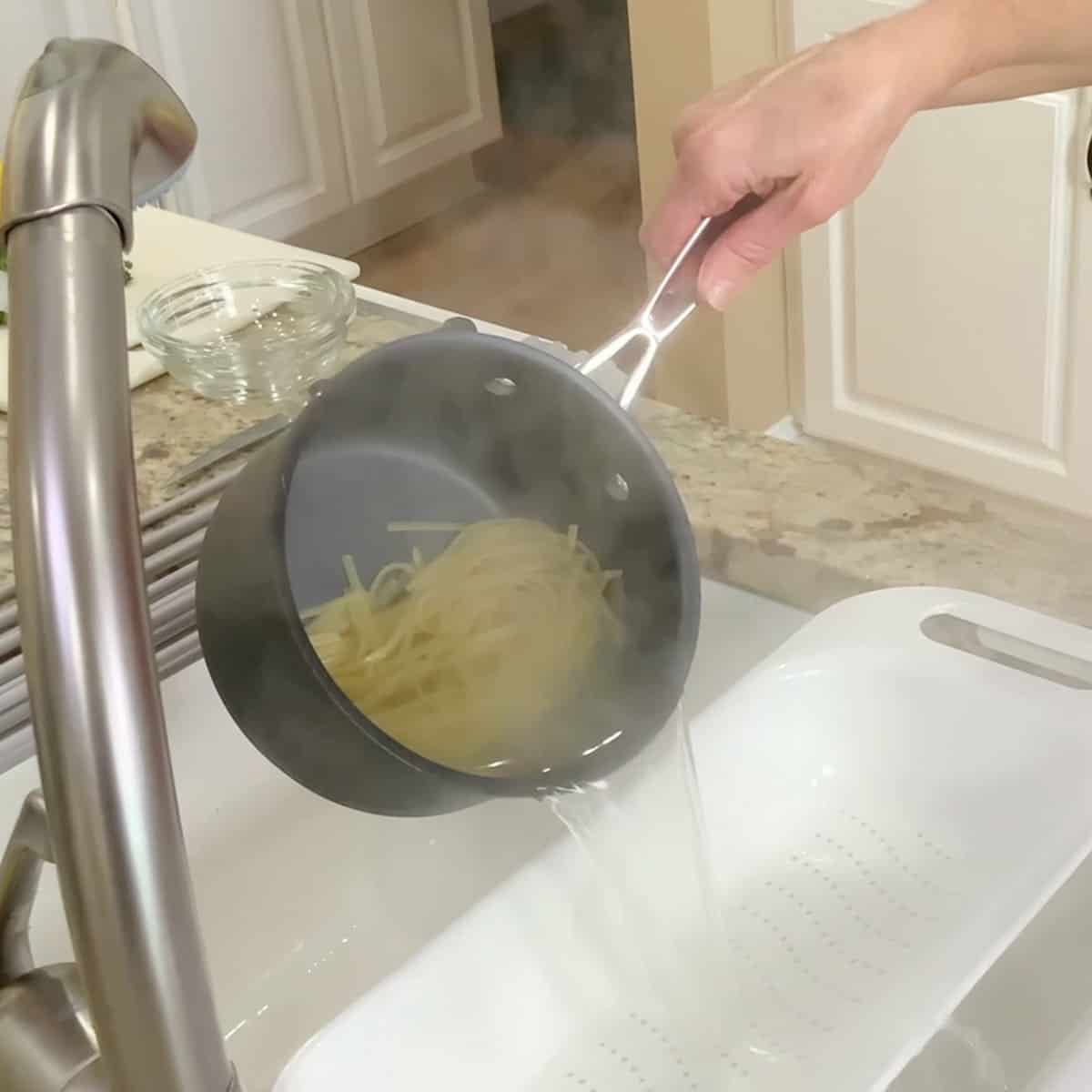 pouring linguini into a colander from a pot