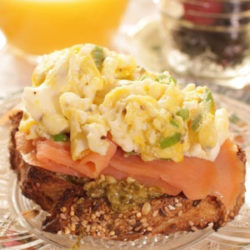 a piece of french bread topped with pesto, smoked salmon and scrambled eggs.