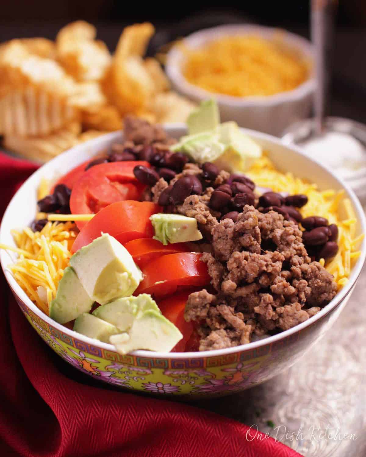 a ground beef taco salad in a bowl next to another bowl of shredded cheese.