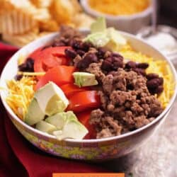 a taco salad next to a bowl of cheese and a bowl of tortilla chips.