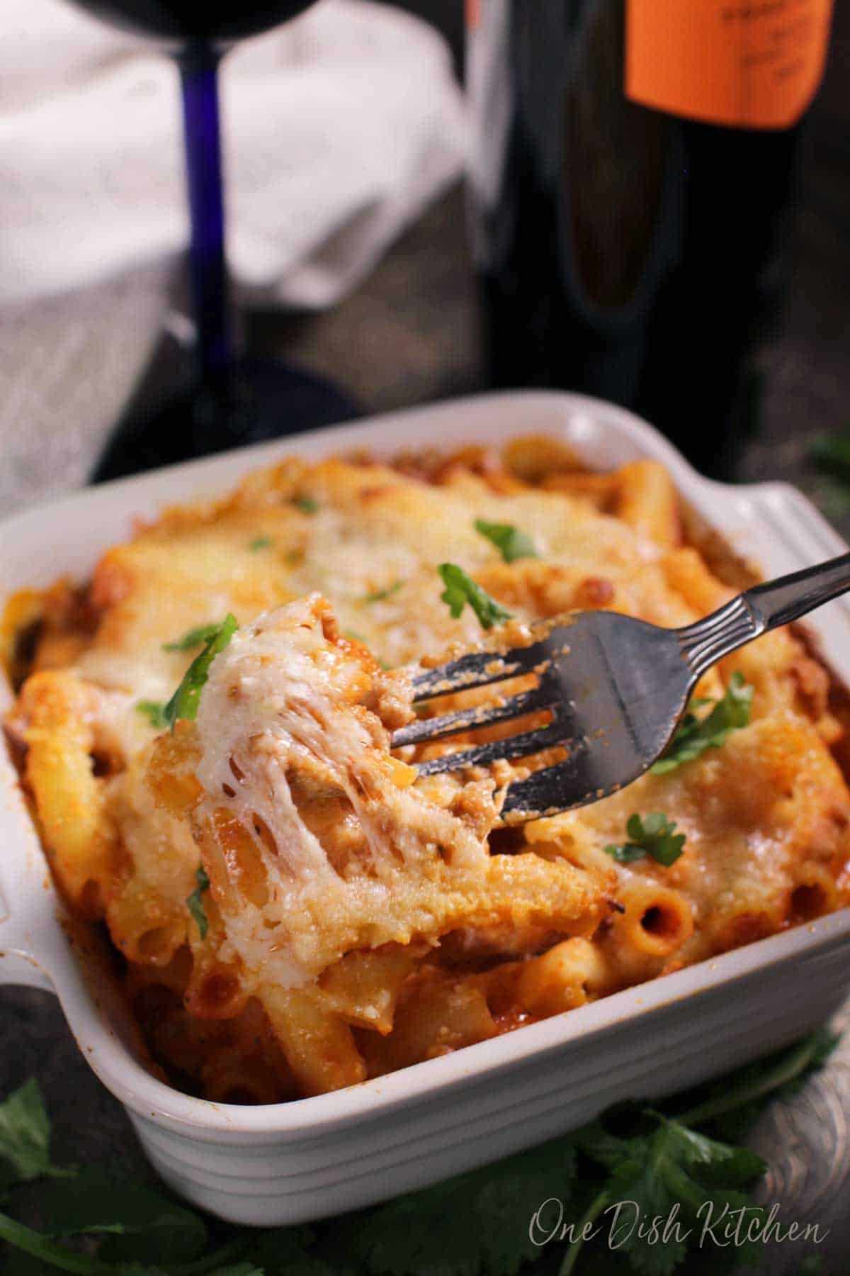 A forkful of a baked ziti casserole with melted cheese hanging from the fork.