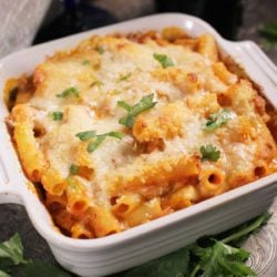 a small baked ziti in a square baking dish next to parsley and a white napkin