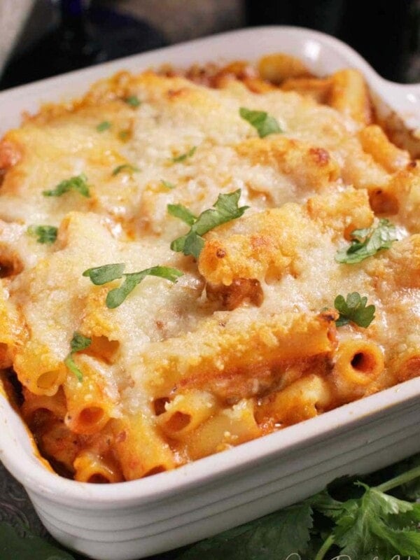 a small baked ziti in a square baking dish next to parsley and a white napkin