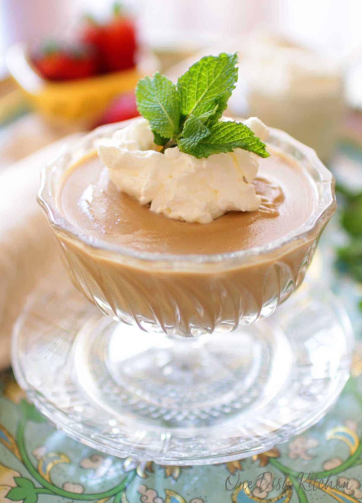 Closeup of butterscotch pudding in a dessert glass topped with whipped cream and mint leaves 