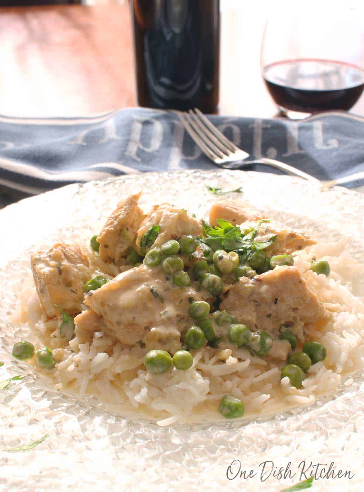 Chicken fricassee served over white rice on a clear glass plate with a blue cloth napkin and a glass of red wine in the background 