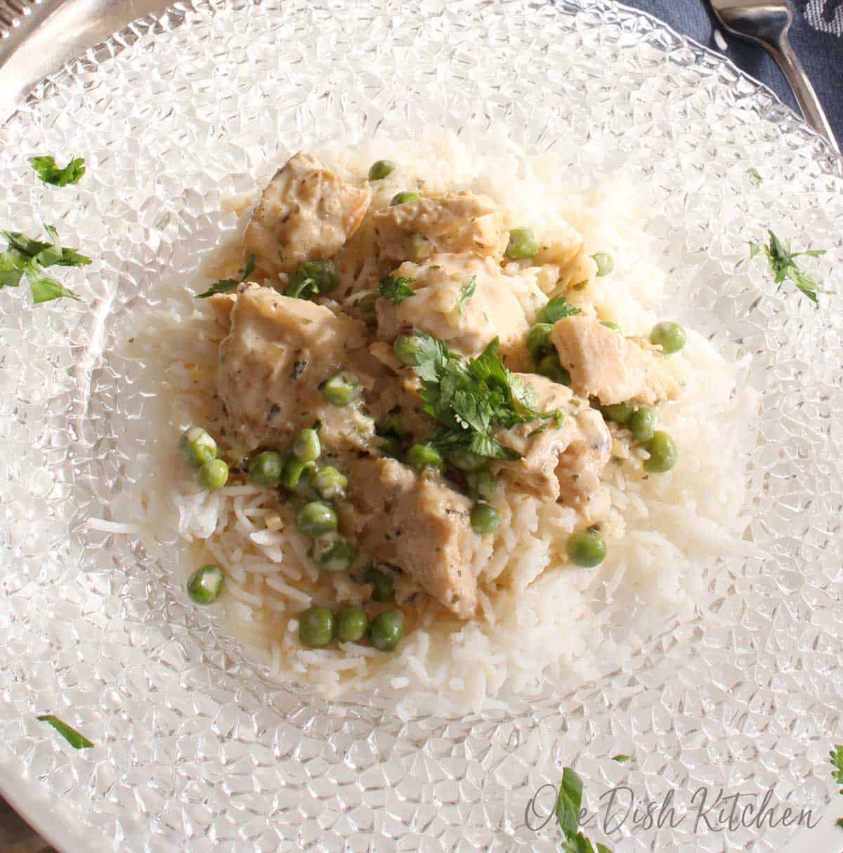 An overhead view of chicken fricassee on a clear glass plate with peas and white rice 