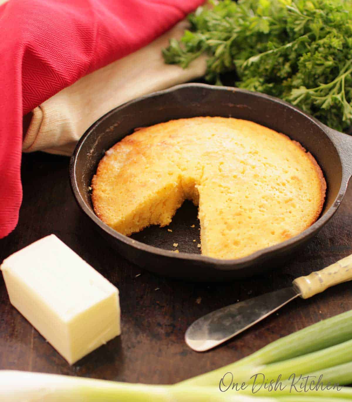 Cornbread in a small cast iron skillet next to a stick of butter and a butter knife.
