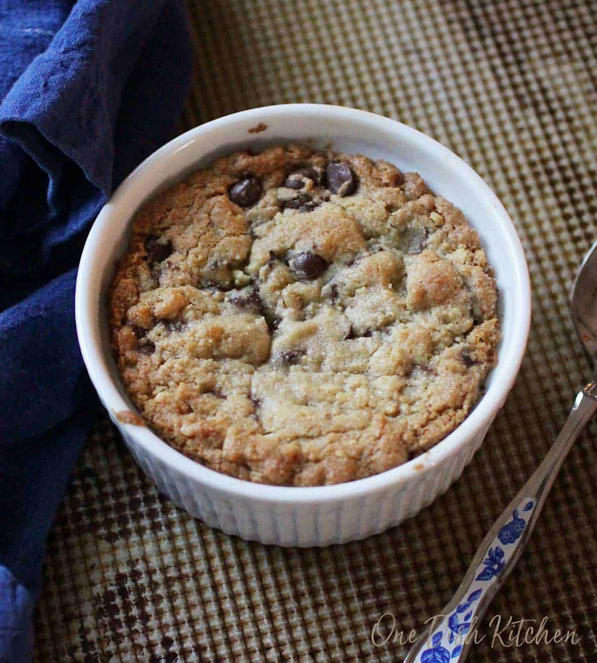 An overhead view of a single chocolate chip cookie on a baking sheet next to a spoon.