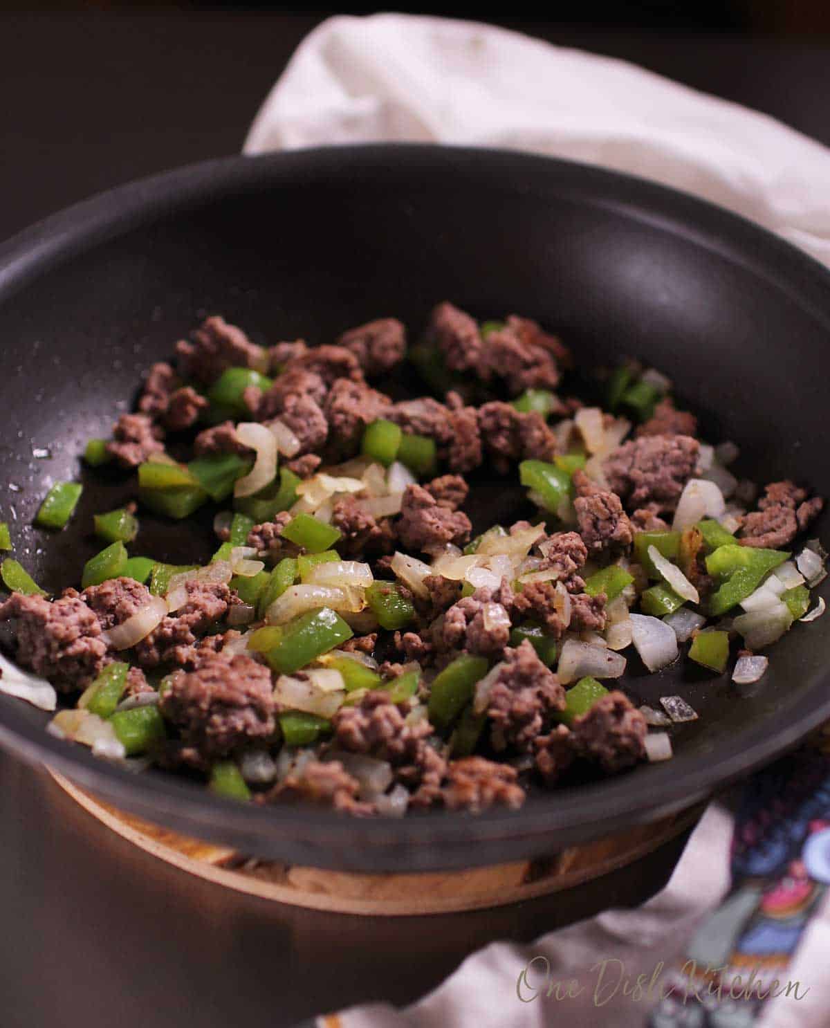 Ground beef, onions, green bell peppers, and garlic cooking in a frying pan.