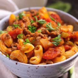 a blue bowl filled with ground beef and elbow macaroni mixed with tomato sauce.