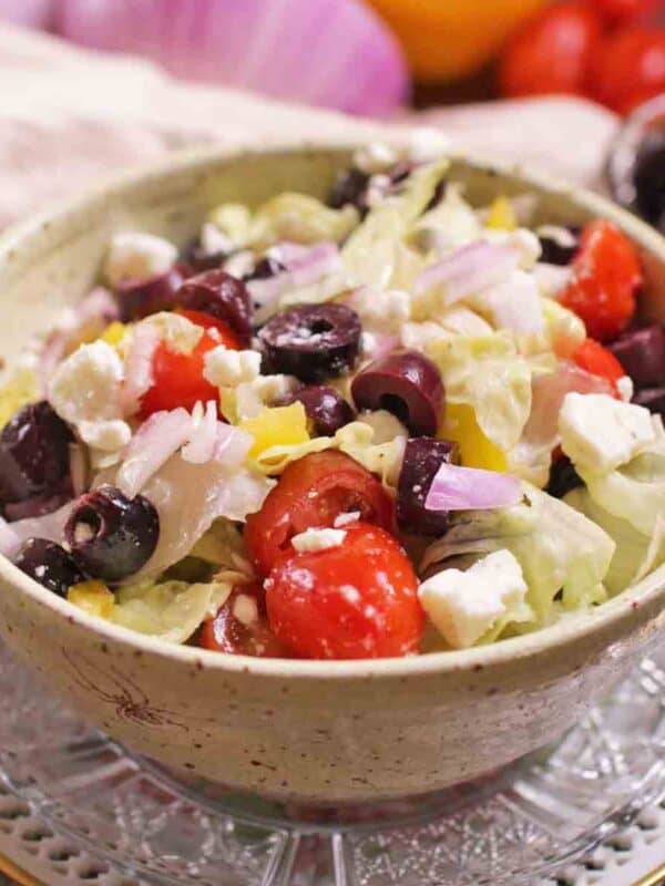 a salad in a yellow bowl filled with tomatoes, olives, red onions, and feta.
