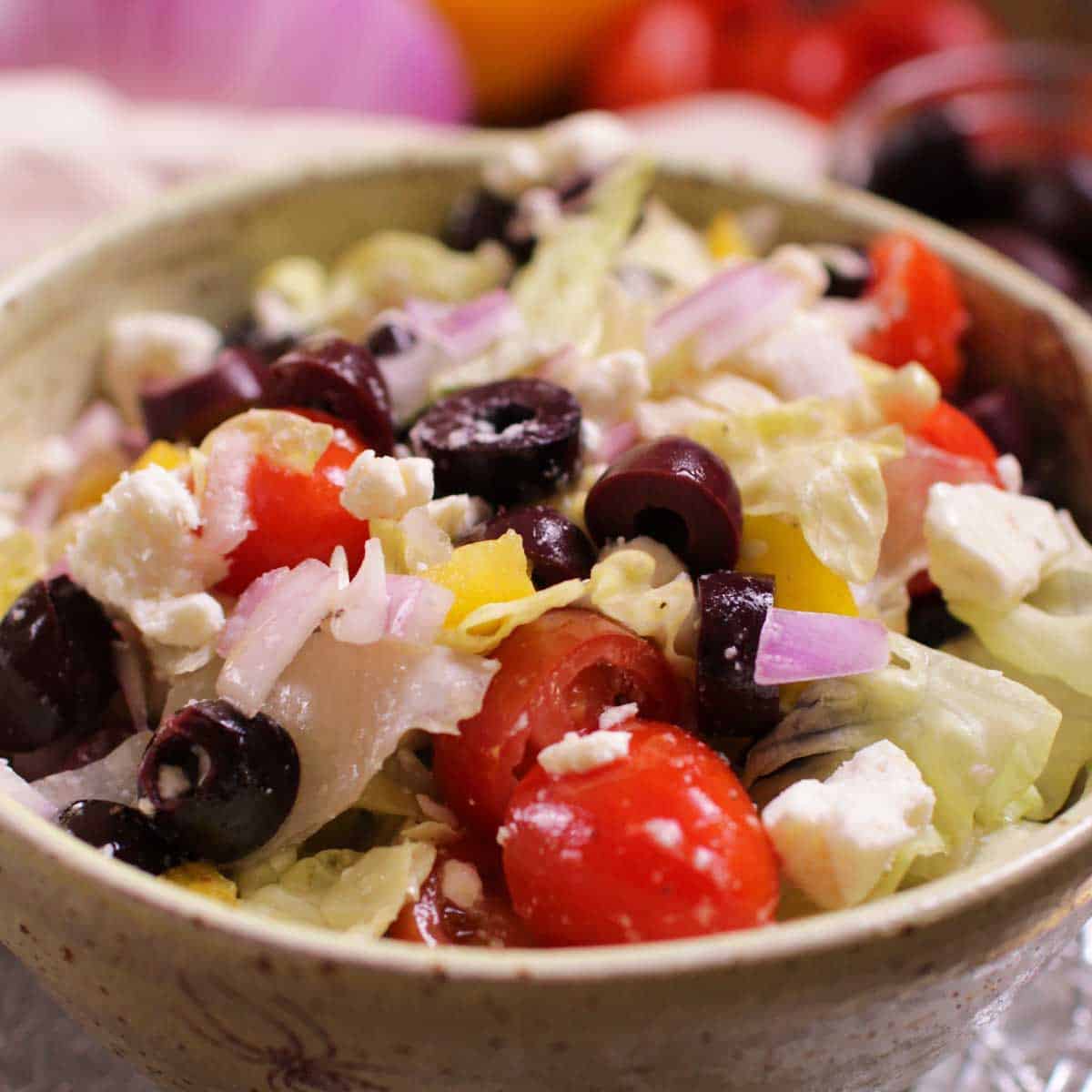 A close up of a Greek salad in a bowl with cherry tomatoes, feta, olives, chopped red onions on a bed of chopped lettuce.