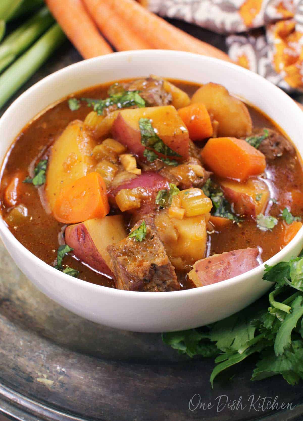 A bowl of irish stew filled with lamb and potatoes next to three carrots.