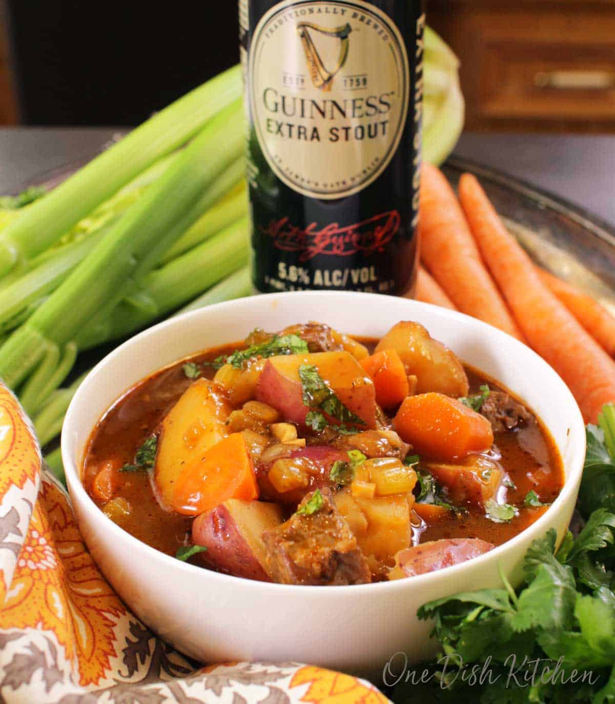 A bowl of irish stew with a can of guinness stout, carrots, and celery in the background.