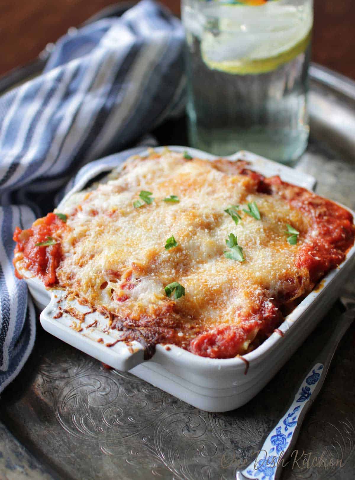 A mini lasagna baked in a small baking dish topped with a layer of melted cheese on a metal tray with a fork.