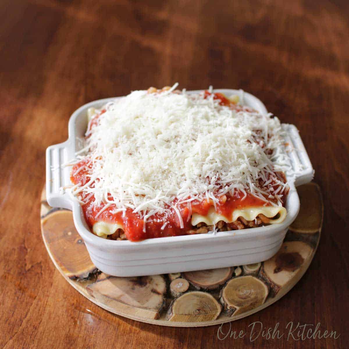 A mini lasagna covered with shredded mozzarella cheese before baking in the oven. 