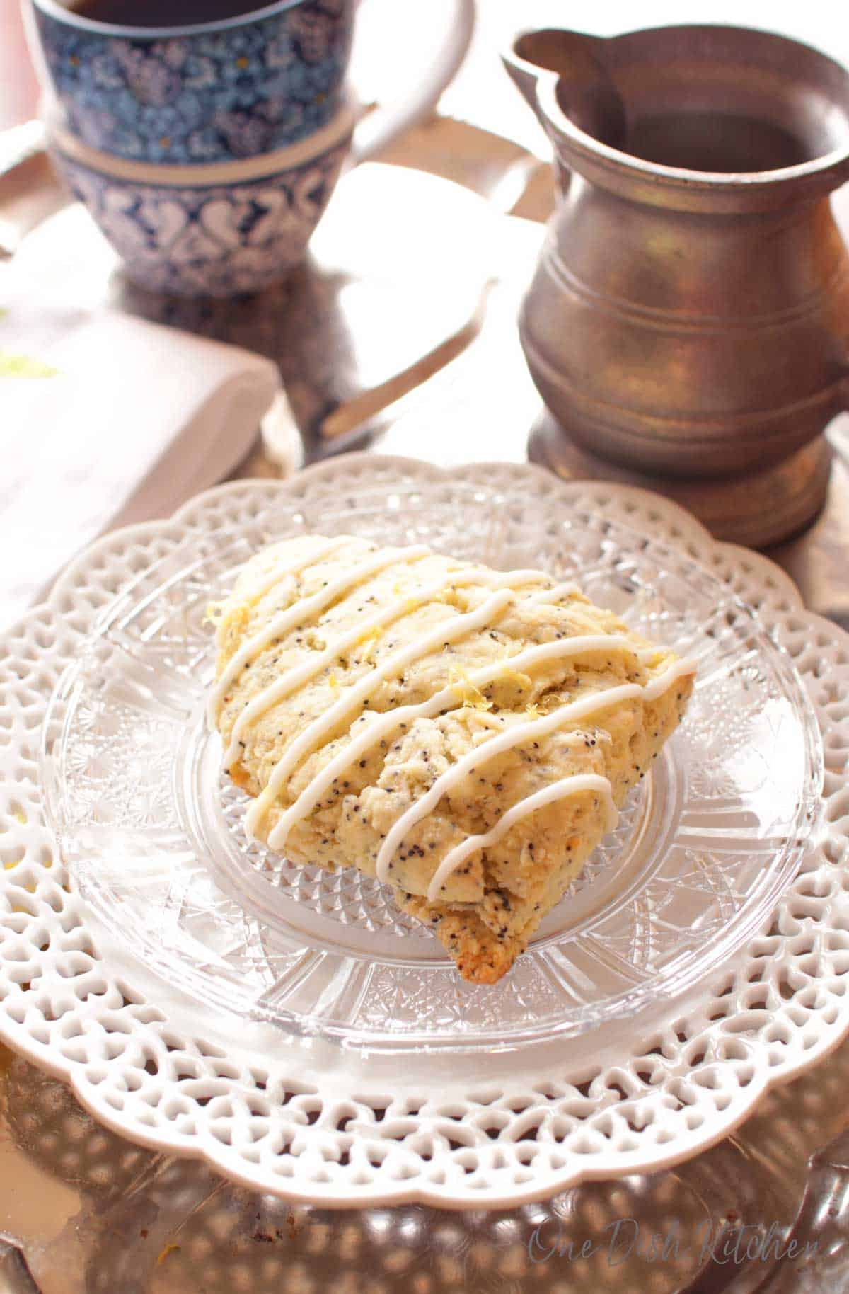 One lemon glazed scone on a plate near a cup of coffee.