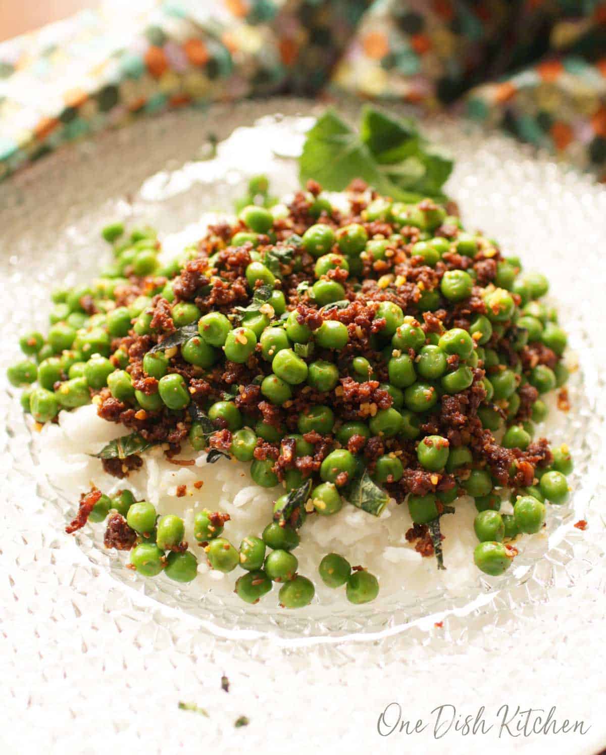 Spicy peas made with chorizo and served over white rice on a clear glass plate.