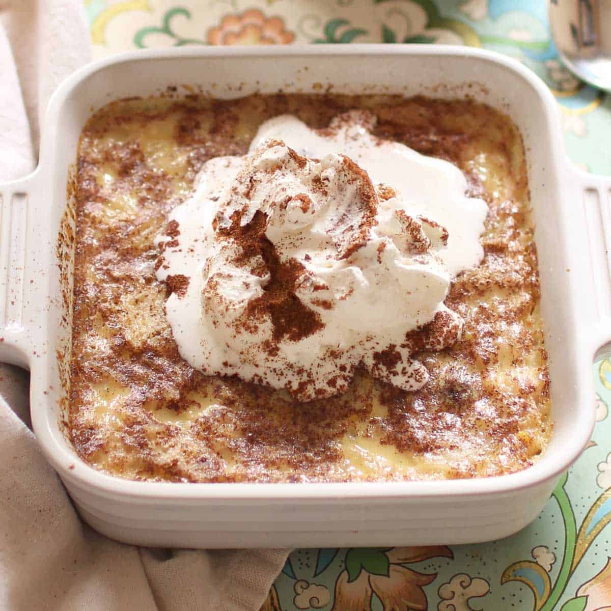 Baked rice pudding topped with whipped cream and ground cinnamon  in small baking dish 