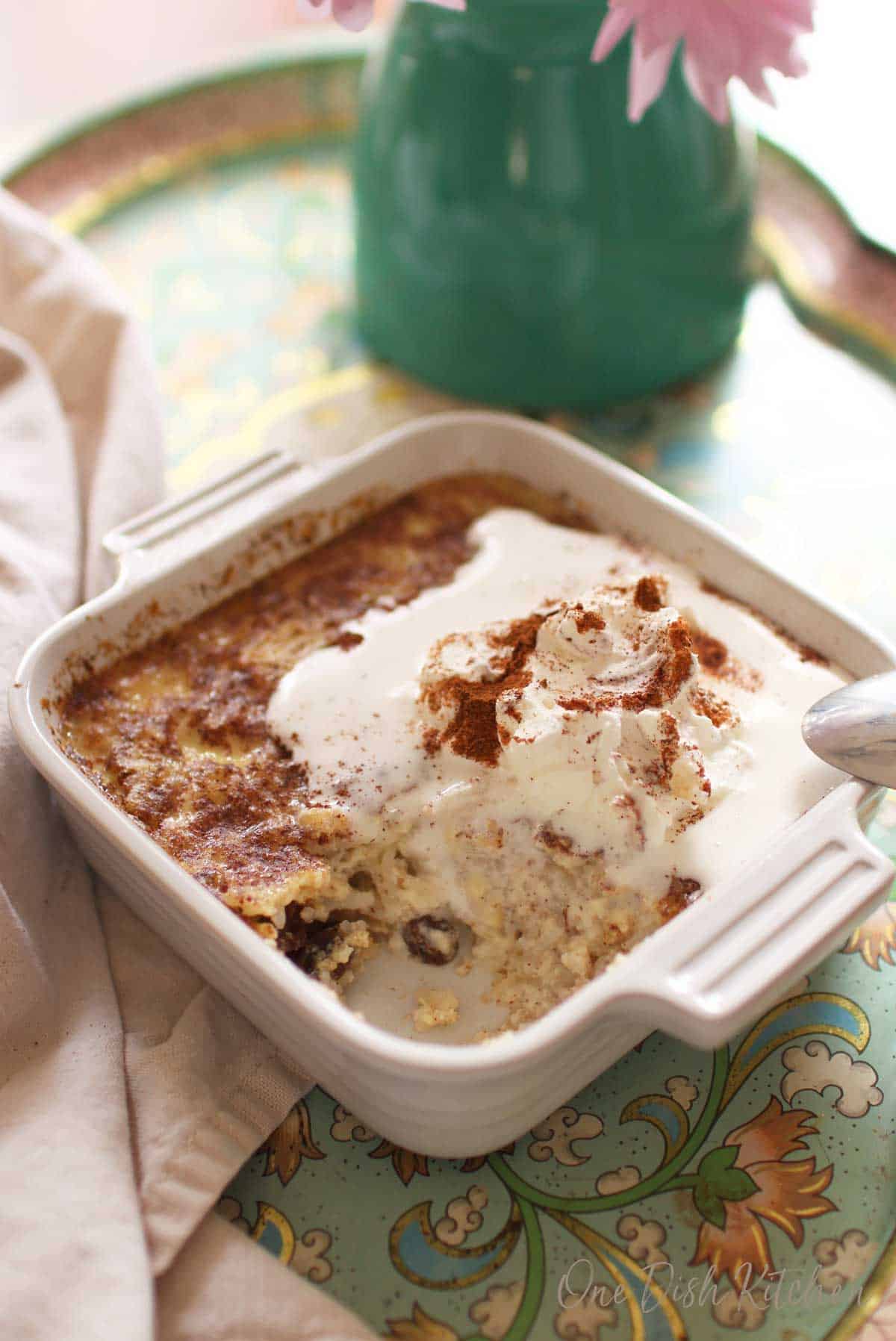A spoonful missing from the homemade rice pudding topped with whipped cream and ground cinnamon in a small baking dish 