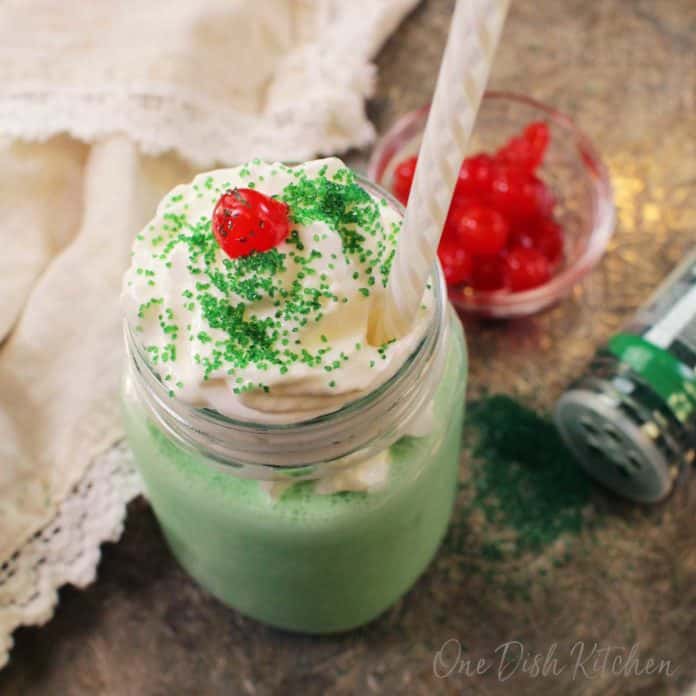 adding a cherry and whipped cream to a shamrock shake.