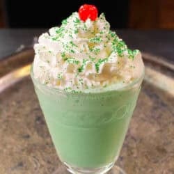 a single shamrock shake in a glass topped with whipped cream, a cherry and sprinkles.