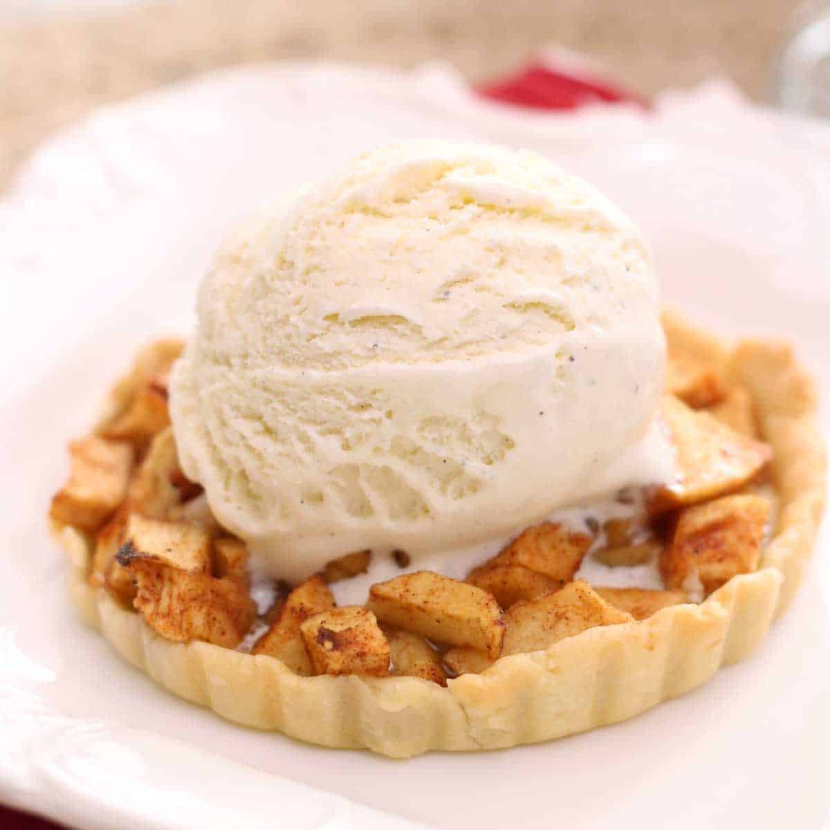A mini apple pie topped with a scoop of vanilla ice cream.