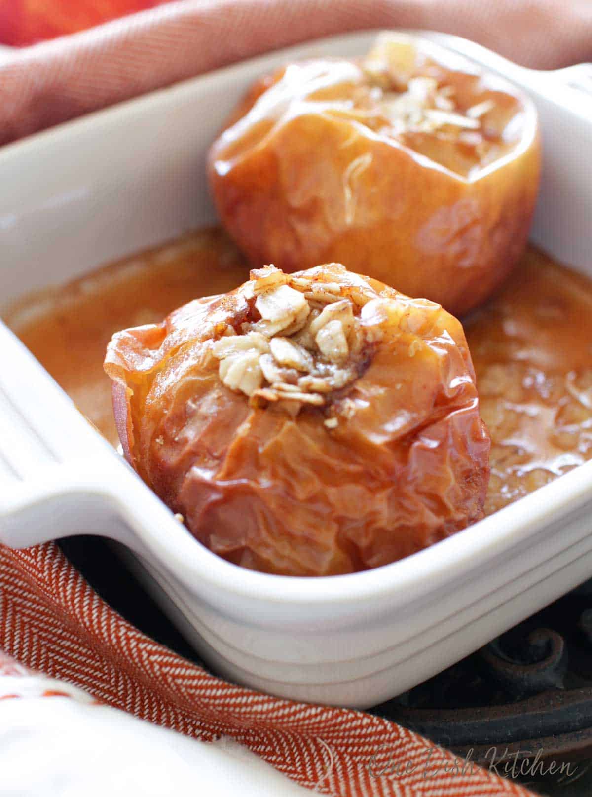 Two baked apples in a small baking dish filled with oats and brown sugar 