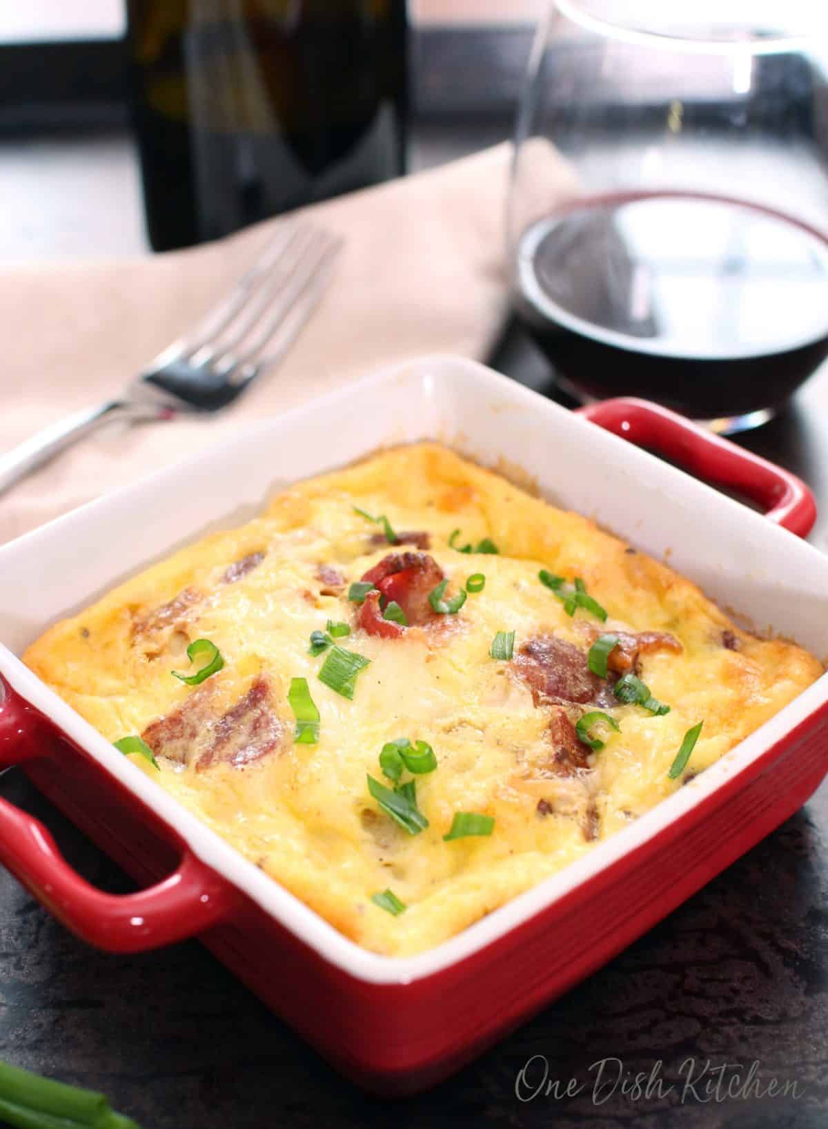 Crustless quiche lorraine baked in a small baking dish on a tray with a glass of red wine.