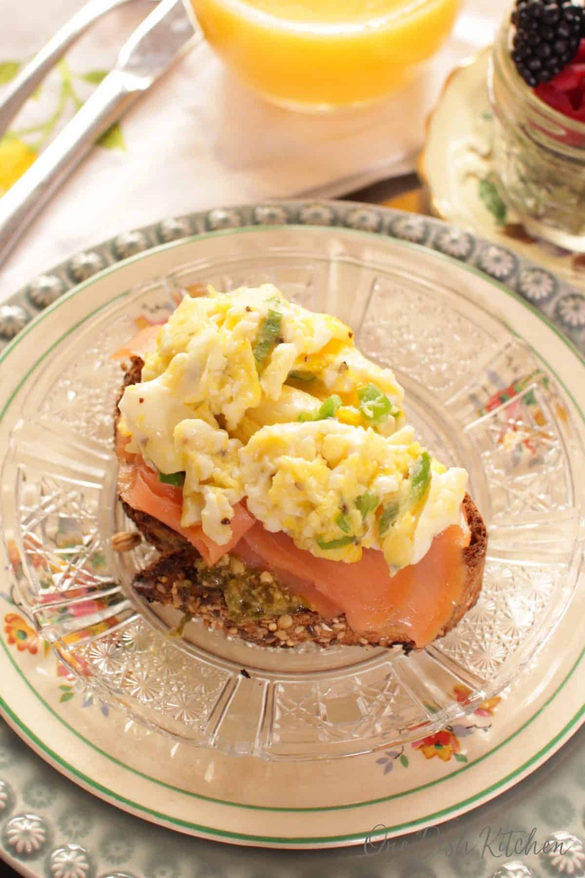An overhead view of a breakfast tray including bread topped with pesto, smoked salmon, and scrambled eggs  