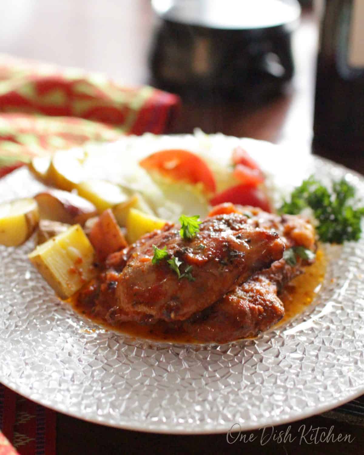 A plate with two chicken thighs in italian sauce and chopped roasted potatoes.
