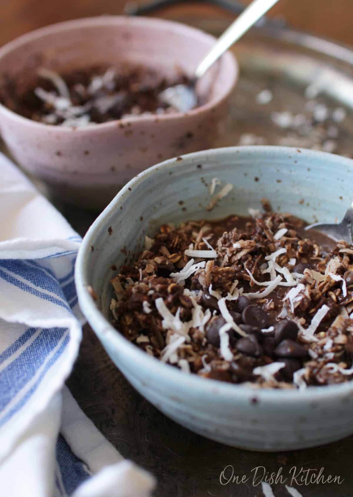 Two mocha oatmeal bowls topped with coconut shavings on a metal tray