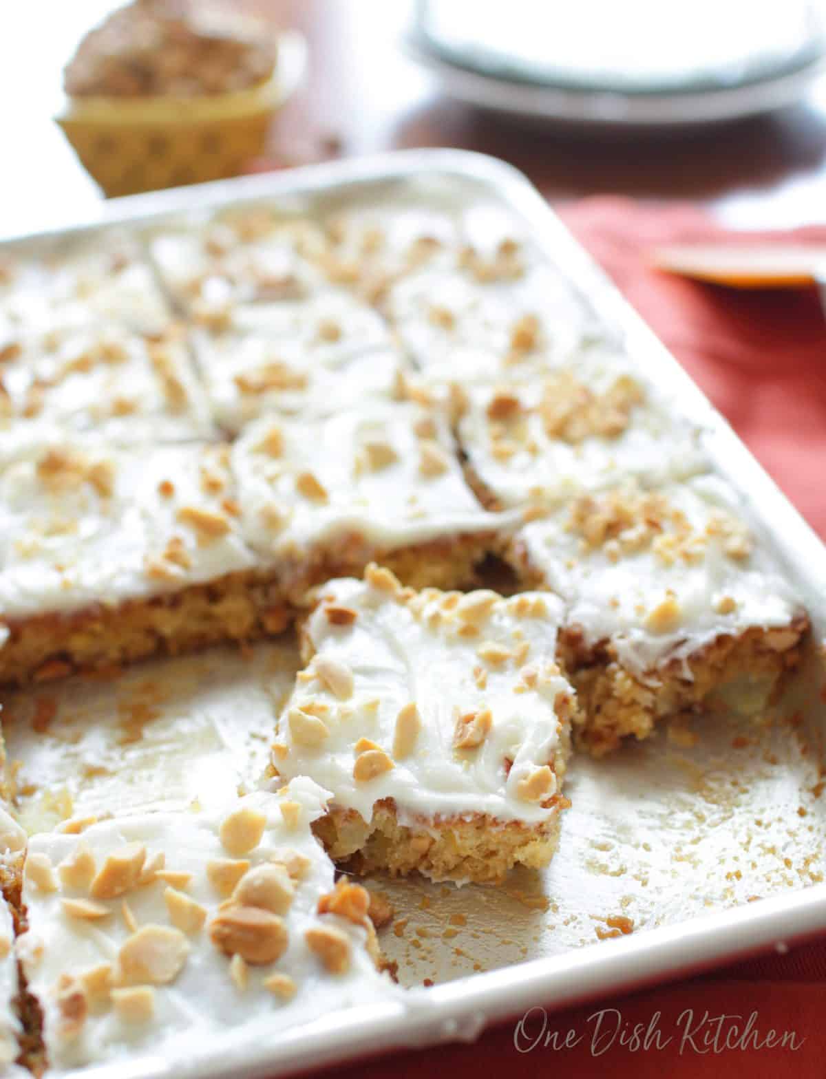 A sheet cake topped with vanilla icing and chopped peanuts cut into squares on a baking sheet.