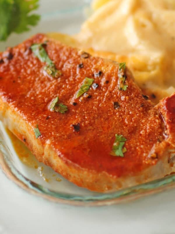 one baked pork chop on a clear plate next to scalloped potatoes and lemon slices.