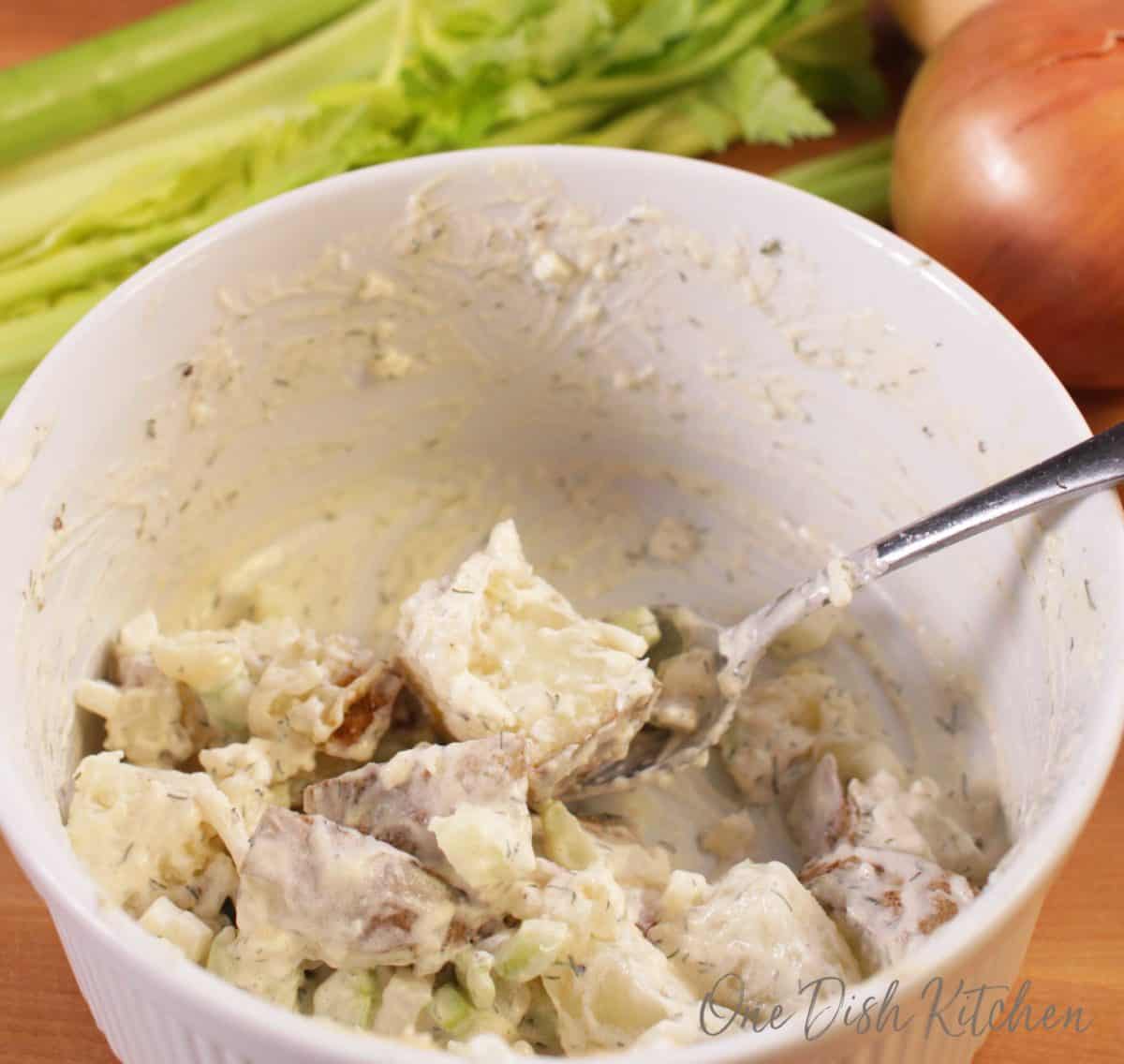 Mixing onions, celery, potatoes, mayonnaise, and mustard together in a small bowl 