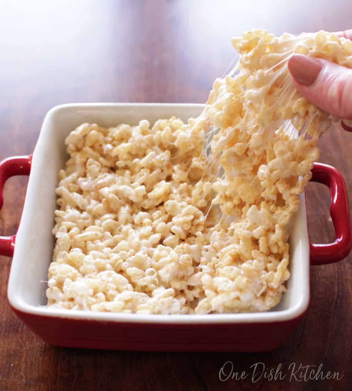 Pulling off a piece of a rice krispie treat with fingers from a small baking dish.
