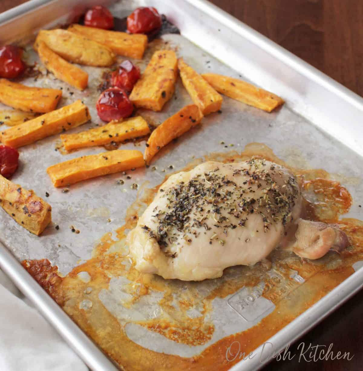 Cooked chicken breast on a pan next to roasted sweet potato slices and cherry tomatoes 