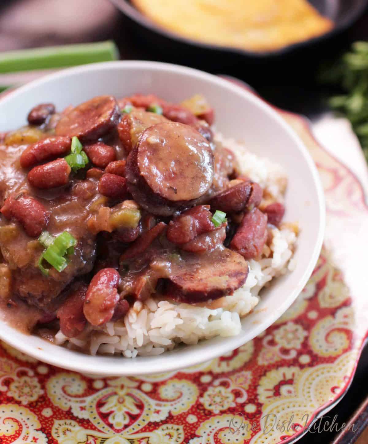 A close up of a bowl of red beans and white rice with sausage.